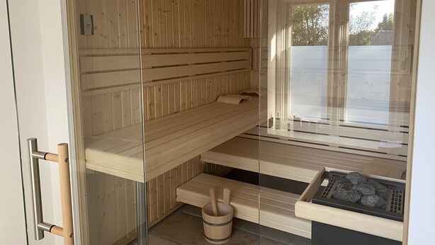 A sauna room with wooden walls, a glass door, a window, and a stone floor. - Reet Kate|3SZ|Sauna|Garding in St. Peter-Ording (Garding, Kirchspiel)