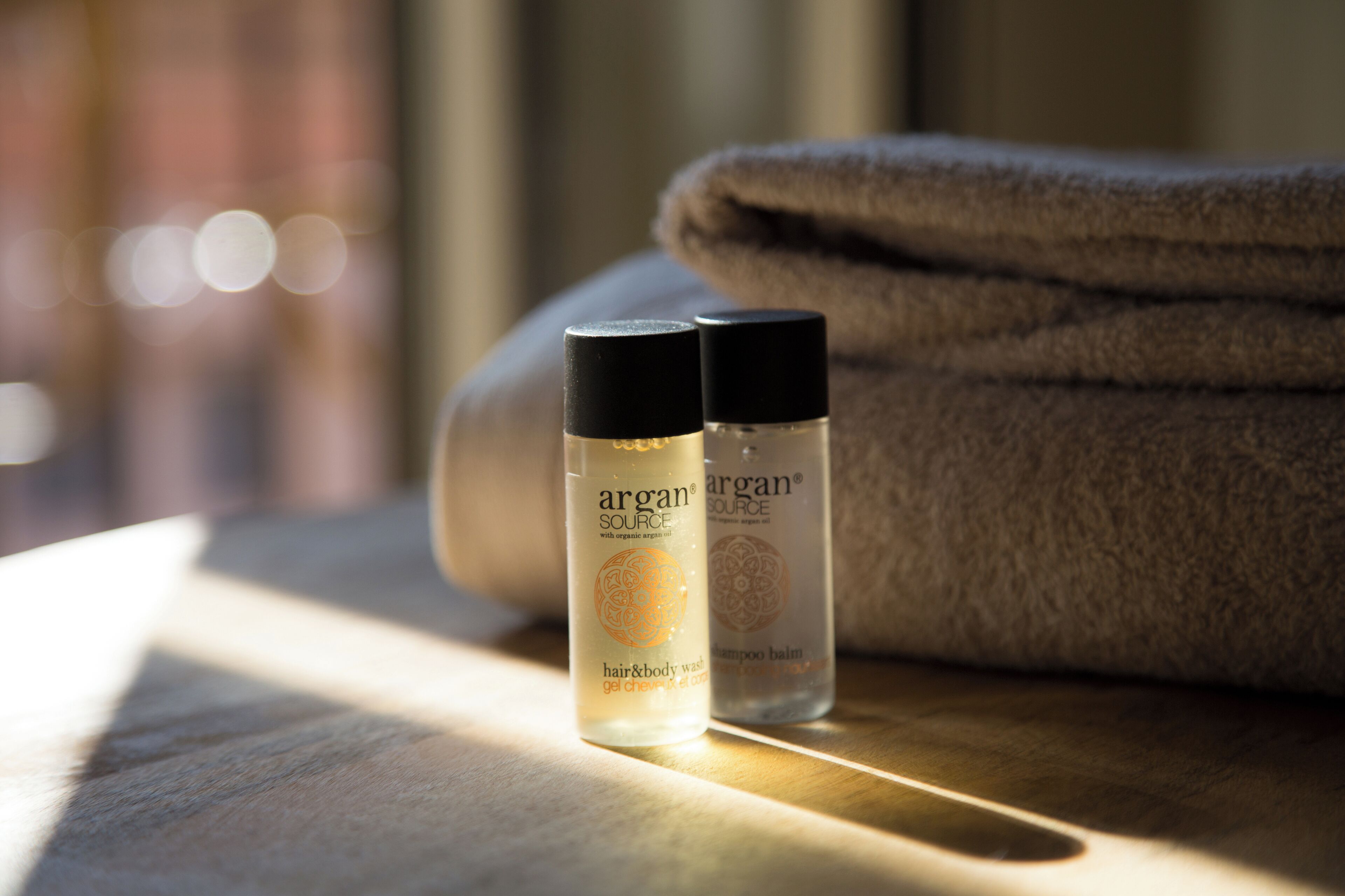 Two bottles of Argan Source hair and body wash and a folded towel on a wooden surface.