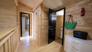 Un intérieur en bois avec un escalier en bois, une porte noire, un meuble blanc et un sac vert accroché au mur.