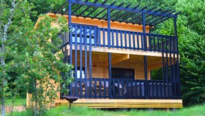 Une cabane en bois à deux étages, dotée d’un balcon et entourée d’arbres.