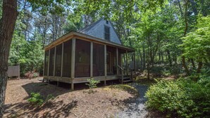 A rustic cabin with a wooden deck, surrounded by dense forest. - Private Location w/ Guest House! (Wellfleet)