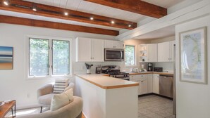 A modern kitchen with white cabinets, a central island, and a wooden ceiling. - Private Location w/ Guest House! (Wellfleet)