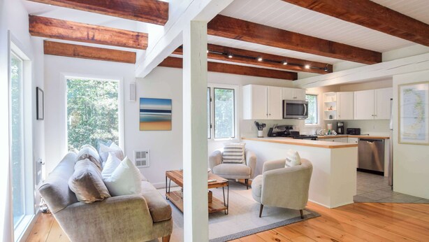 A spacious living area with a wooden ceiling, a kitchen with white cabinets, and a large window providing natural light. - Private Location w/ Guest House! (Wellfleet)