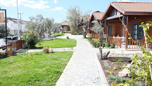 Un sendero lleva a cabañas de madera con tejados de tejas, rodeadas de jardines cuidados y árboles.