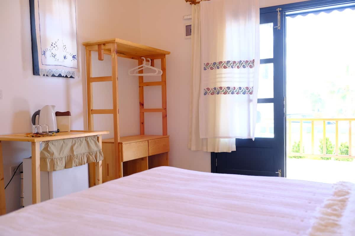Une chambre à coucher avec un lit, un bureau en bois, une bouilloire et une fenêtre avec des rideaux.