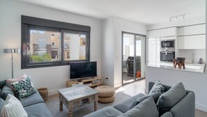 Un salon moderne avec un canapé, une table basse et un téléviseur. Une porte-fenêtre coulissante donne accès à un balcon.