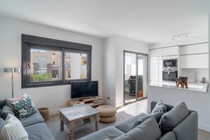 A modern living room with a sofa, a coffee table, and a TV. There is a sliding glass door leading to a balcony.