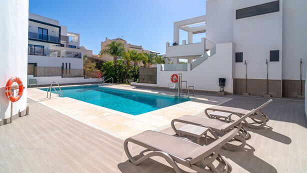 Une piscine avec des chaises longues, une bouée de sauvetage et un ciel bleu azur.