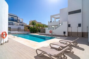 Une piscine avec des chaises longues, une bouée de sauvetage et un ciel bleu azur.