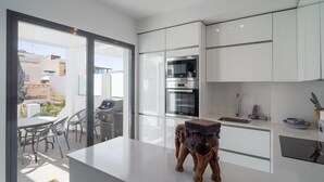 Une cuisine moderne avec des meubles blancs, un four encastré et un coin repas avec des sièges à l’extérieur.
