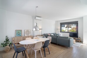 Un salon moderne comprenant un coin repas, un canapé gris, un téléviseur à écran plat et une grande fenêtre.