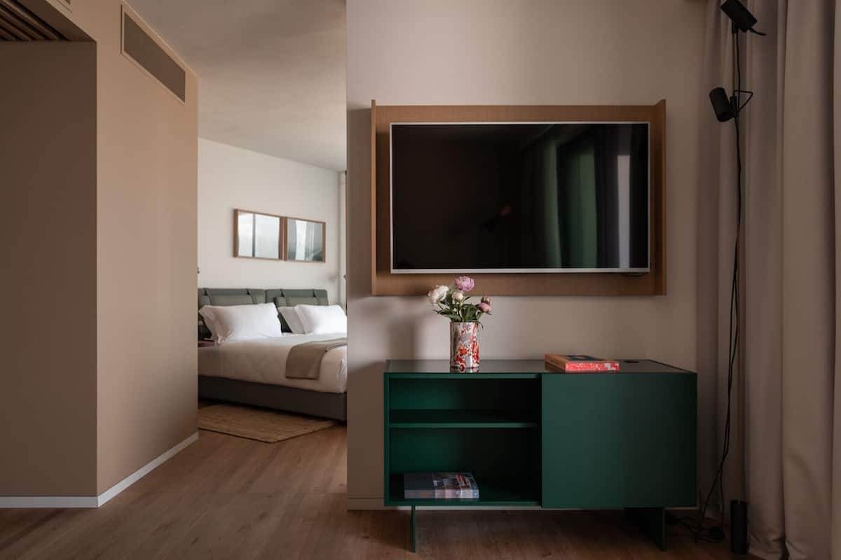 A modern hotel room with a bed, a green console table, a large mirror, and a wall-mounted TV.
