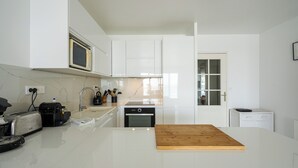 Una cocina moderna con armarios blancos, un microondas, un tostador y una tabla de cortar de madera en la encimera.