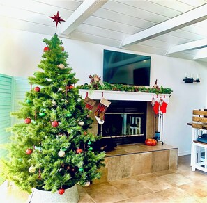 A living room with a Christmas tree, a fireplace, and a TV mounted on the wall. - Enchanting Cottage with Sweeping Lake Views, Golden Sunsets, Hot Tub, Nature Trail & Dog-Friendly (Blue Eye)