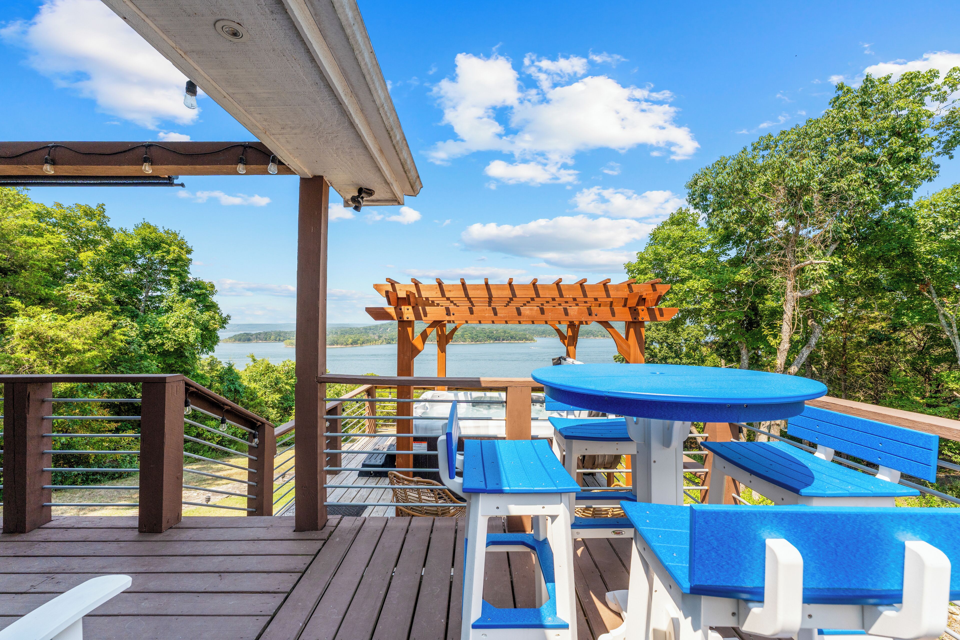 Eine Holzterrasse mit blauer und weißer Gartenmöbeln, einer Pergola und Blick auf einen See.