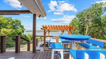 Eine Holzterrasse mit blauer und weißer Gartenmöbeln, einer Pergola und Blick auf einen See.