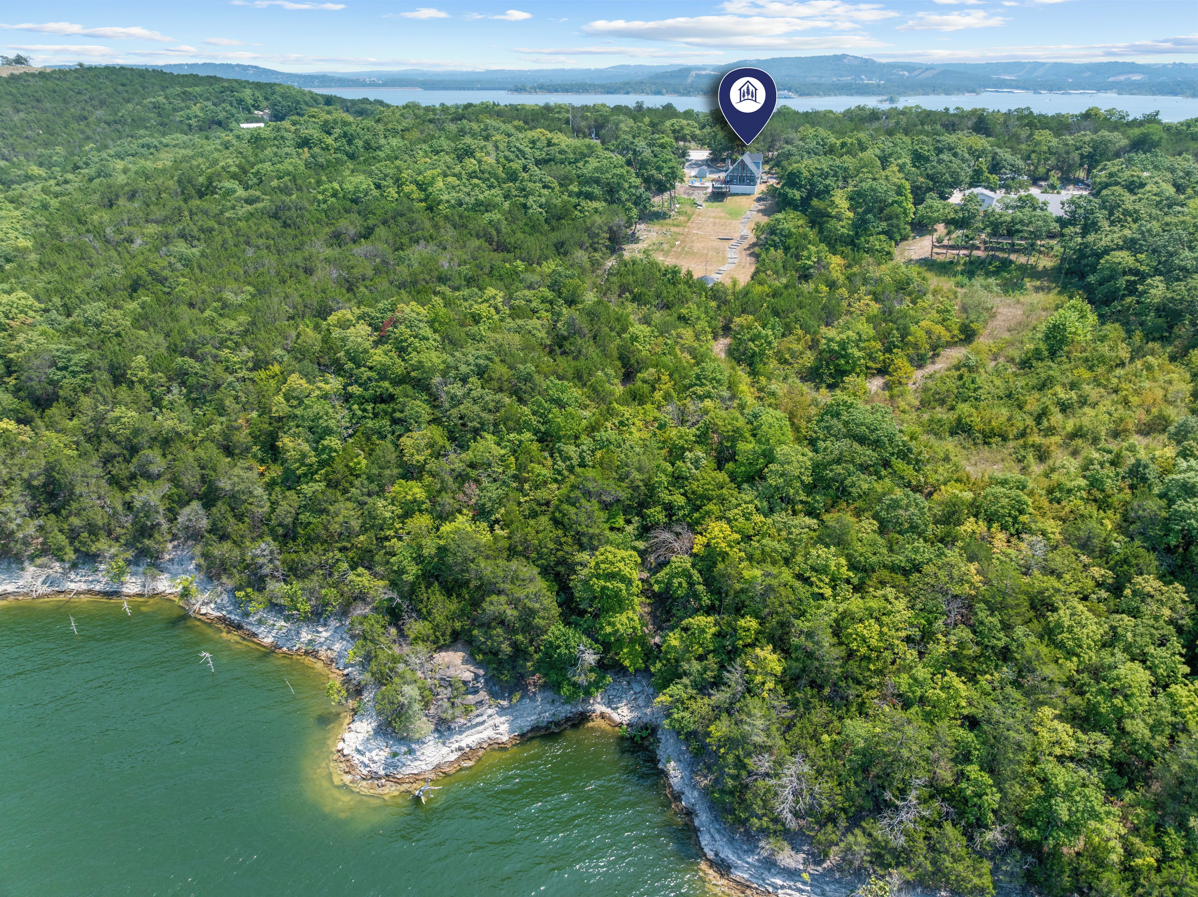 An aerial view of a forested area with a building surrounded by trees and a body of water.