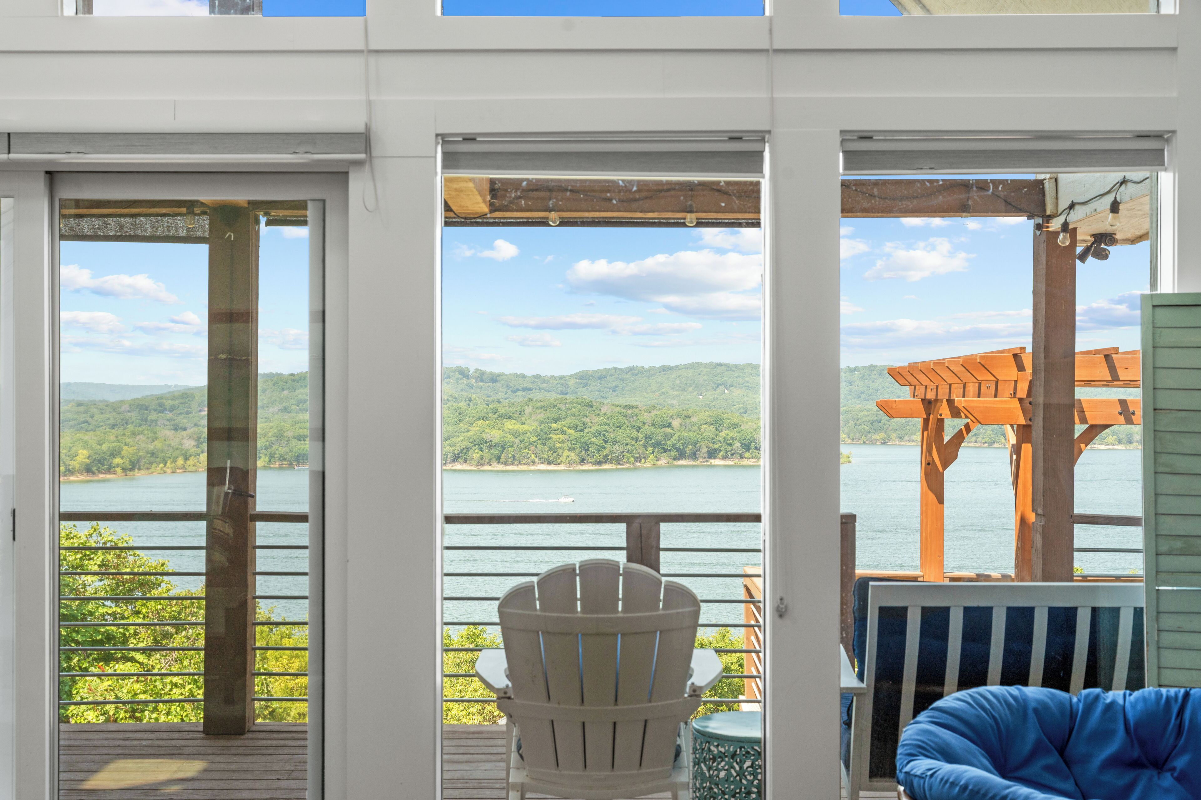 Eine Terrasse mit Blick auf einen See und Hügel, mit einem weißen Adirondack-Sessel und einem blauen Sitzsack.