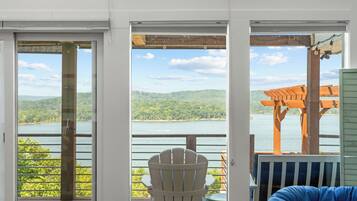 Eine Terrasse mit Blick auf einen See und Hügel, mit einem weißen Adirondack-Sessel und einem blauen Sitzsack.