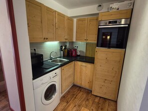 A compact kitchen with wooden cabinets, a washing machine, and a built-in oven.