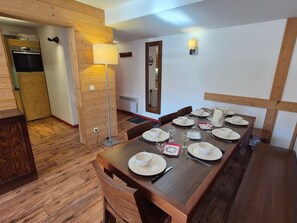 A dining area with a wooden table set for four, a lamp, and a kitchen in the background.