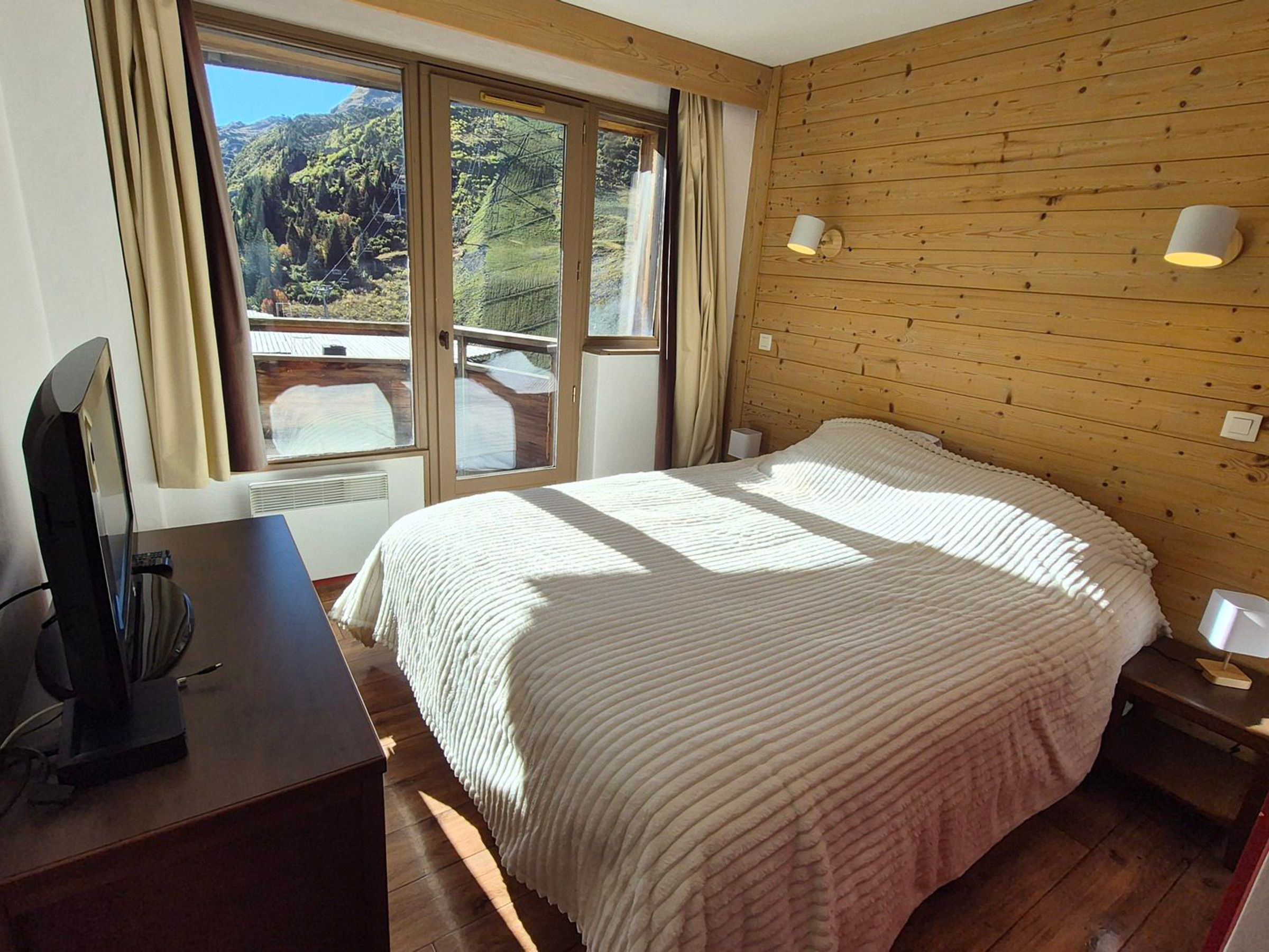 Un dormitorio con una cama grande, un escritorio con ordenador, una ventana con cortinas y una pared de madera.