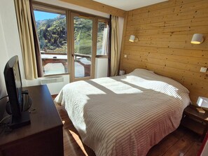 A bedroom with a large bed, a desk with a computer, a window with curtains, and a wooden wall.