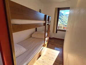 A bunk bed room with a wooden headboard, a small table, and a window with a mountain view.