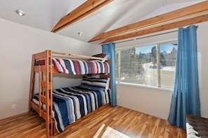 A bunk bed room with wooden beams, a window with curtains, and a view of the outside. - Clouds Rest Cabin by Destination Big Bear: Tranquil Secluded Setting with Ski Slope Views! Close to Hiking Trails! Foosball! (Big Bear City)