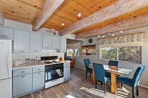 A modern kitchen with white cabinets, a central island, and a dining area with blue chairs.