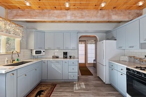 A kitchen with light blue cabinets, a microwave, a stove, and a refrigerator. - Clouds Rest Cabin by Destination Big Bear: Tranquil Secluded Setting with Ski Slope Views! Close to Hiking Trails! Foosball! (Big Bear City)