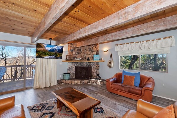 A cozy living room with a stone fireplace, leather furniture, and a large TV mounted on the wall.