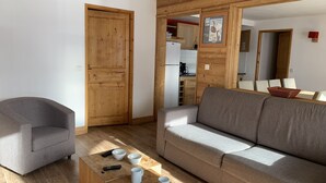 Ein Wohnzimmer mit grauem Sessel, grauem Sofa und einem Holztisch mit Fernbedienungen und Tassen.