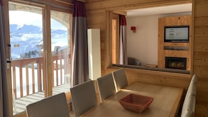 Ein Holzinnenraum mit einem Esstisch, Stühlen, einem Fernseher und Blick auf eine verschneite Landschaft.