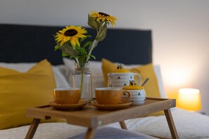 A wooden tray with a vase of sunflowers, two teacups, and a teapot with bee designs on a bed with yellow pillows and a nightlight. - Ocean Waves - Ground Floor Apartment Pet Friendly Enclosed Garden (Saundersfoot)