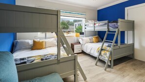 A bedroom with bunk beds, a window with a view, and a bedside table with a lamp. - Ocean Waves - Ground Floor Apartment Pet Friendly Enclosed Garden (Saundersfoot)