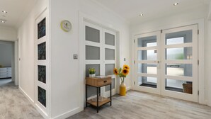 A spacious room with a wooden floor, a desk with a vase of sunflowers, and frosted glass doors. - Plas Gwyn - Walk to Beach Parking Enclosed Garden (Saundersfoot)