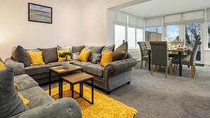 A modern living room with a grey sofa set, yellow cushions, a wooden coffee table, and a yellow rug. - Plas Gwyn - Walk to Beach Parking Enclosed Garden (Saundersfoot)