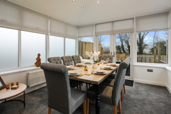 A dining room with a large table set for six, surrounded by grey upholstered chairs.