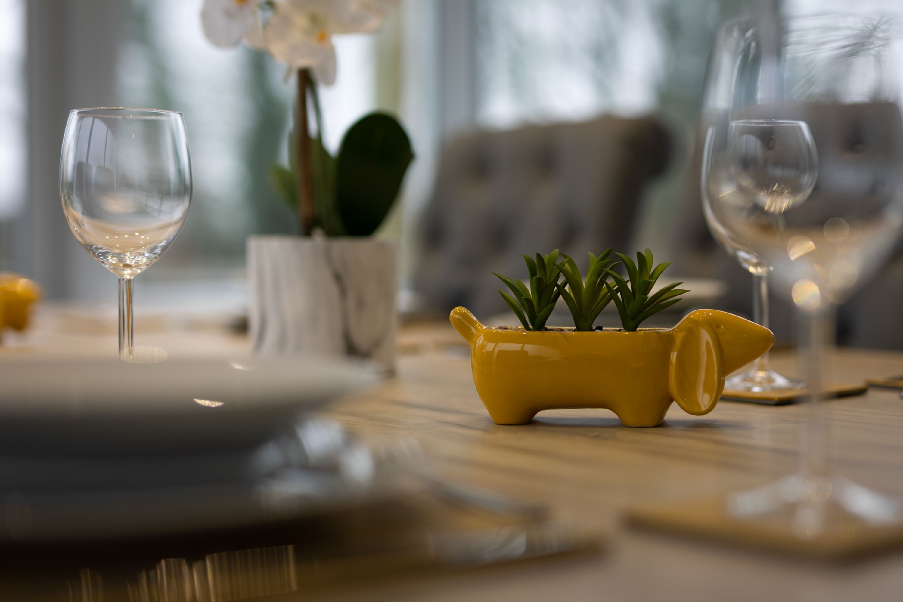 Een eettafel met twee wijnglazen en een gele pot met groene planten.