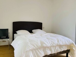 Una cama individual con cabecera oscura en una habitación con suelo de madera y un pequeño escritorio con silla.