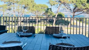 A dining table with four chairs and wine glasses, set against a backdrop of trees and a clear sky. - 3-room apartment, 2 beds, beach, parking, AC, WiFi (Calvi)