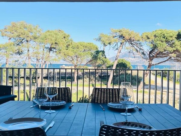 A dining table with four chairs and wine glasses, set against a backdrop of trees and a clear sky. - 3-room apartment, 2 beds, beach, parking, AC, WiFi (Calvi)