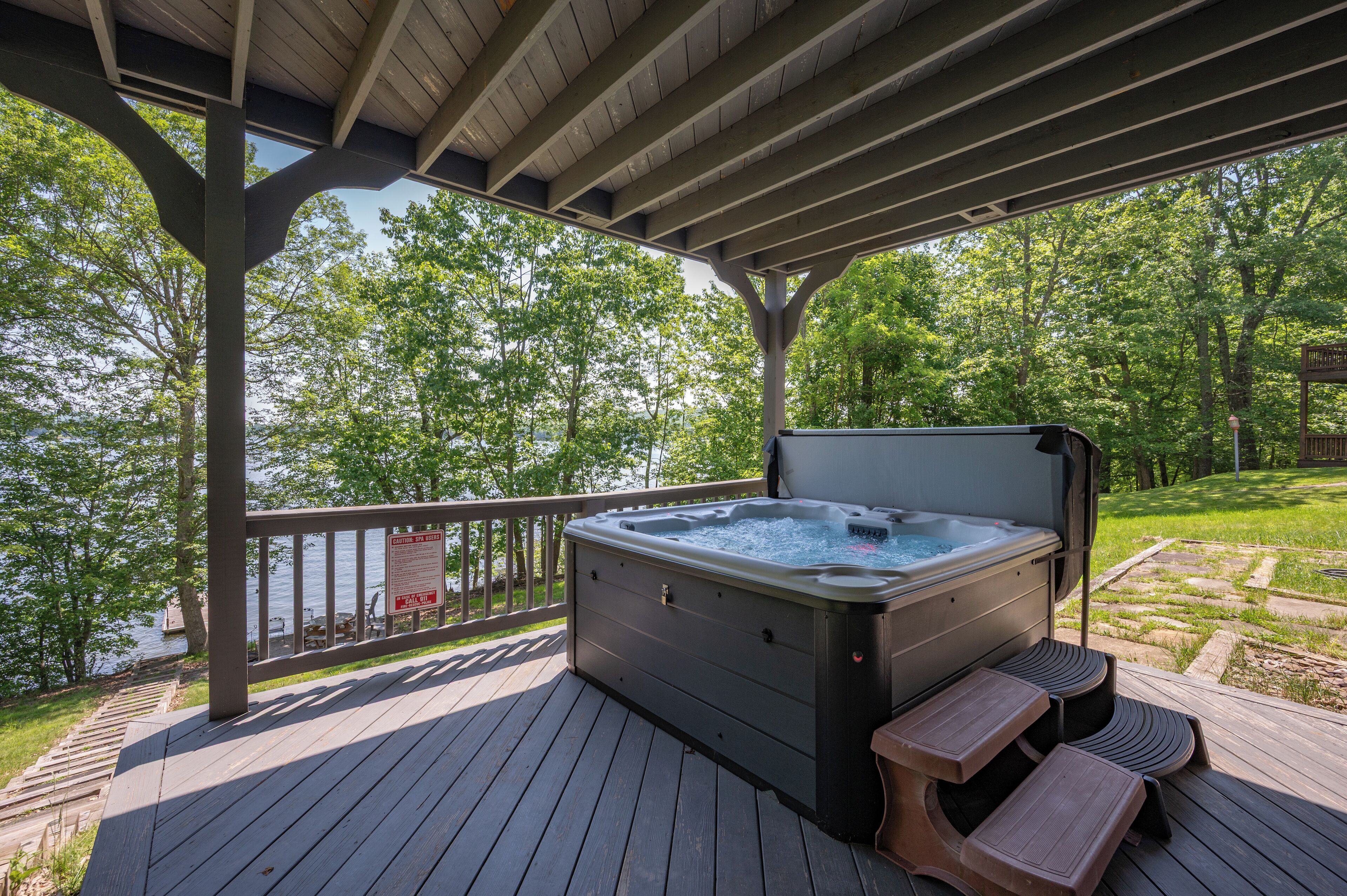 A hot tub on a wooden deck with a view of a lake and trees.