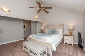 A bedroom with a bed, bedside tables, a bench, a ceiling fan, and a heater.