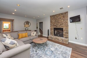 A living room with a stone fireplace, a sofa with patterned cushions, a round coffee table, and a mounted TV.