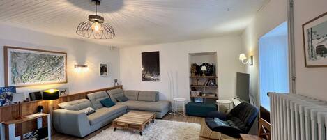 A modern living room with a sectional sofa, a wooden coffee table, a fluffy rug, a rocking chair, and a TV.