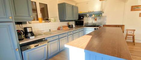 A kitchen with blue cabinets, a wooden countertop, a built-in stove, and a hanging light fixture.