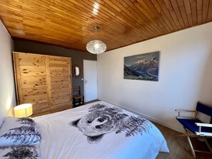 Ein Schlafzimmer mit Holzboden, einem Bett mit einer großen Bettdecke mit Tiermotiv, einem Gemälde von Bergen und einem Klappstuhl.