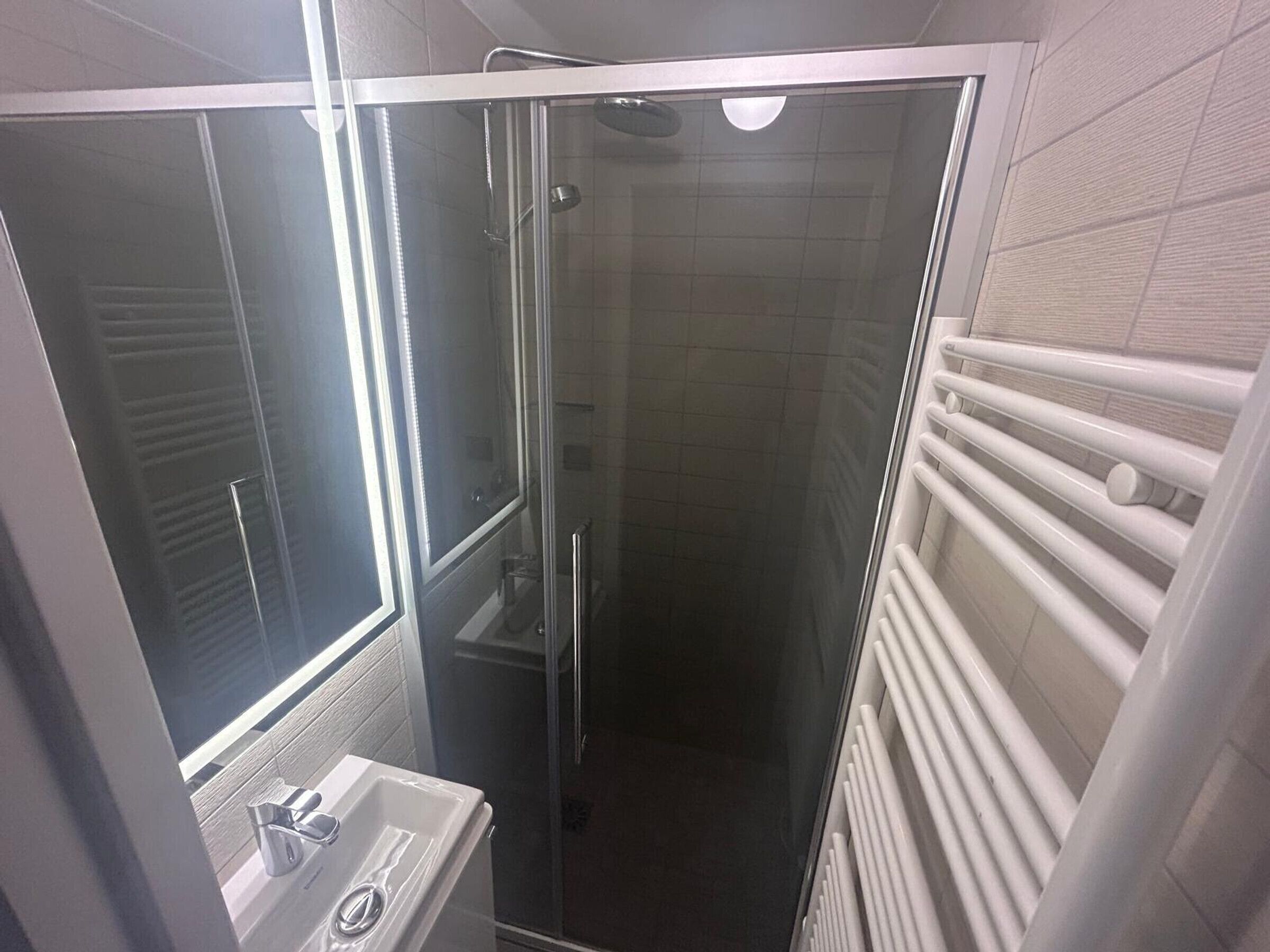 A bathroom with a glass shower enclosure, a sink, and a white towel rack.
